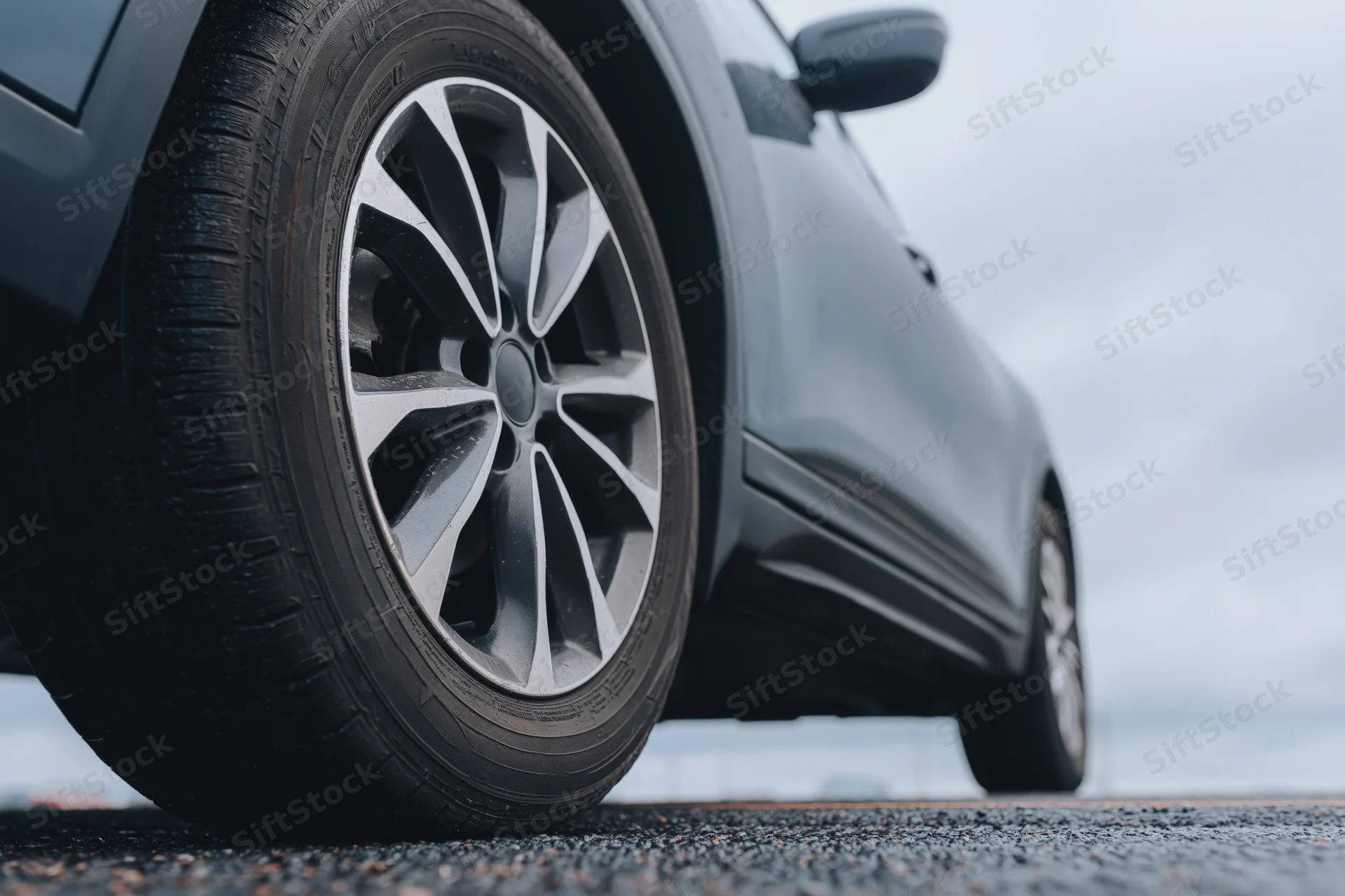 Close-up of a dark gray suv's front wheel and alloy rim on asphalt road