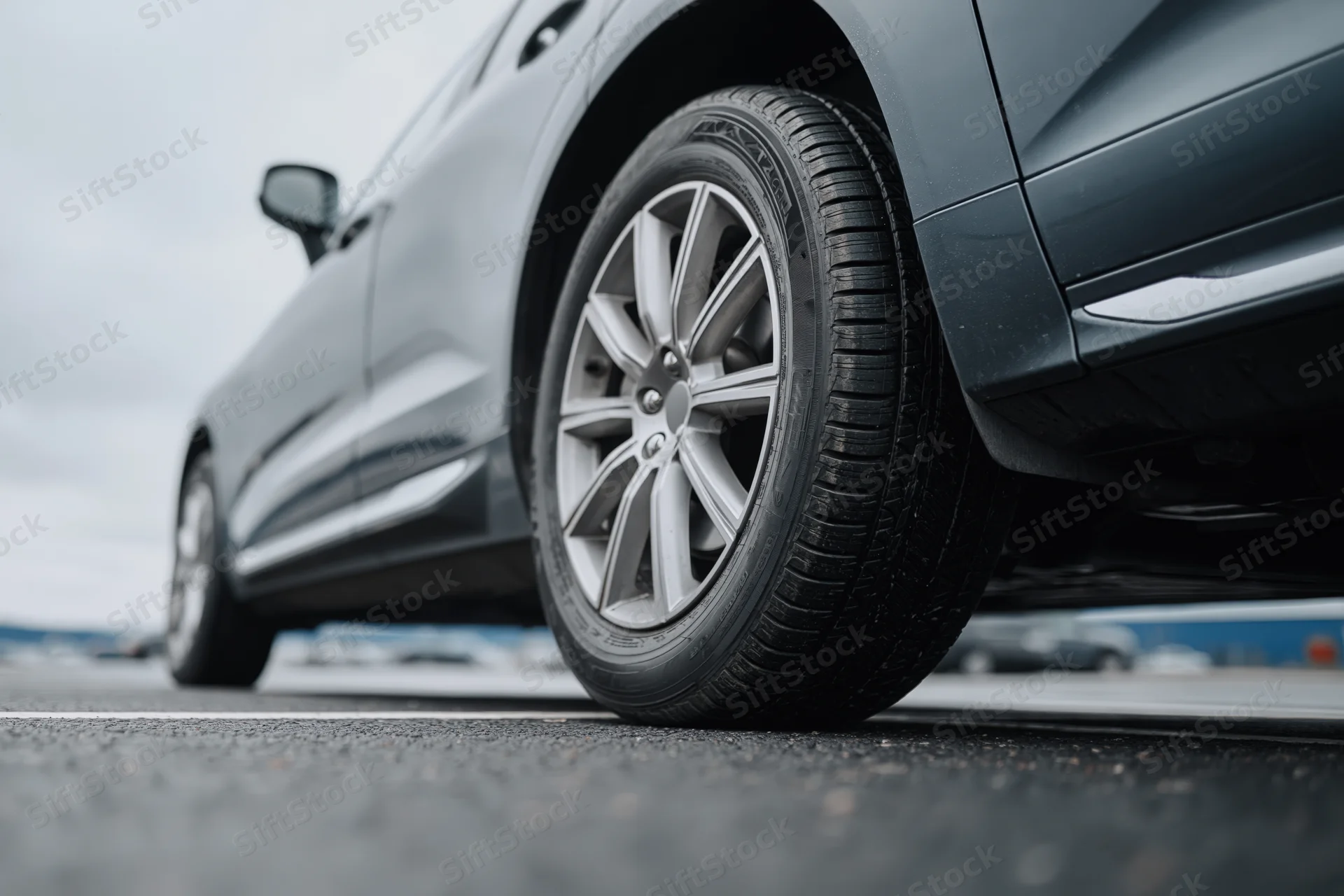 Low-angle close-up of a dark grey suv's front wheel and alloy rim on asphalt road