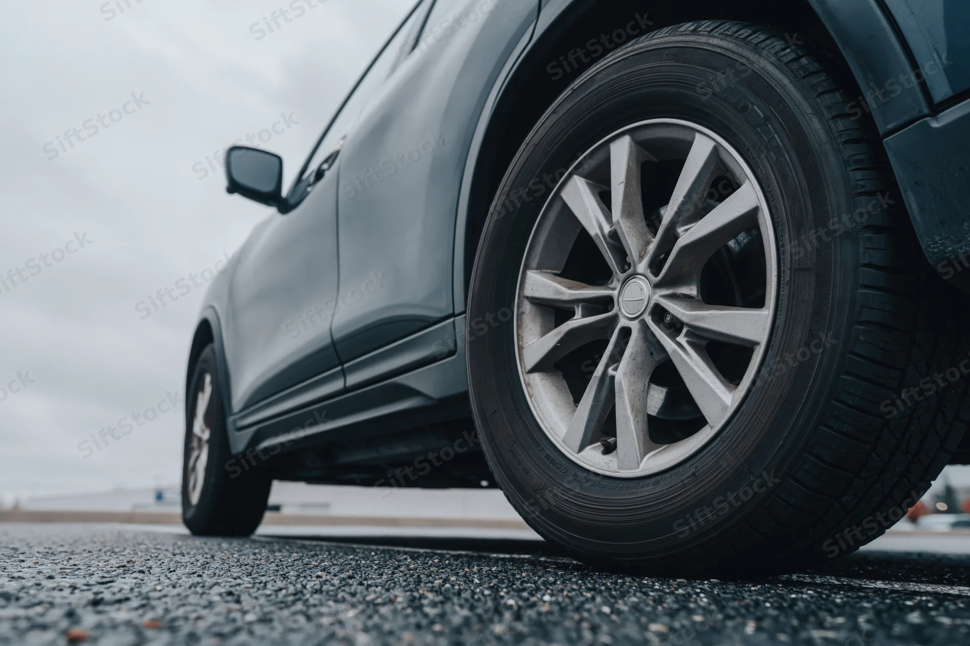 Low-angle close-up of a dark grey suv's front wheel and alloy rim on asphalt road