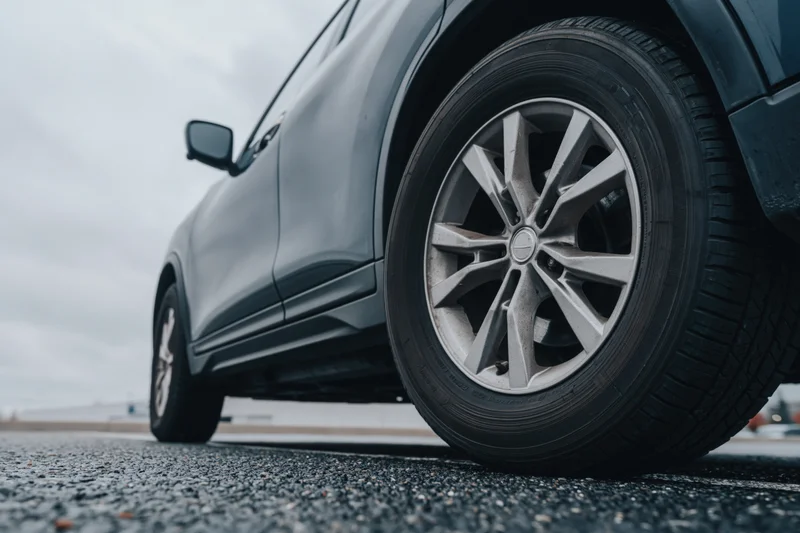 Low-angle close-up of a dark grey suv's front wheel and alloy rim on asphalt road