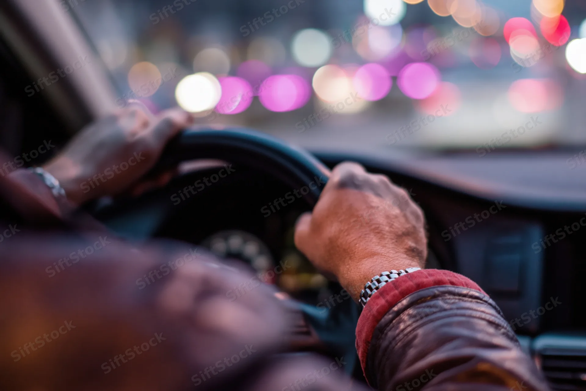 Man’s hands gripping steering wheel while driving through city at night