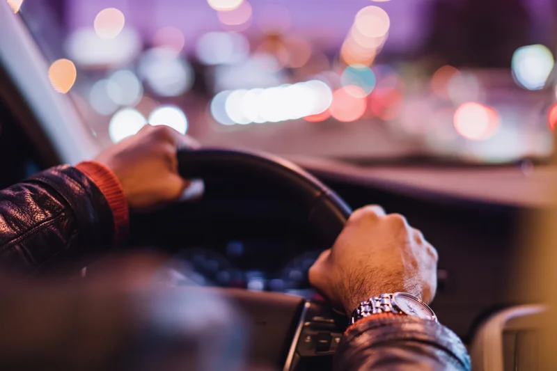 Man’s hands gripping steering wheel while driving through city at night