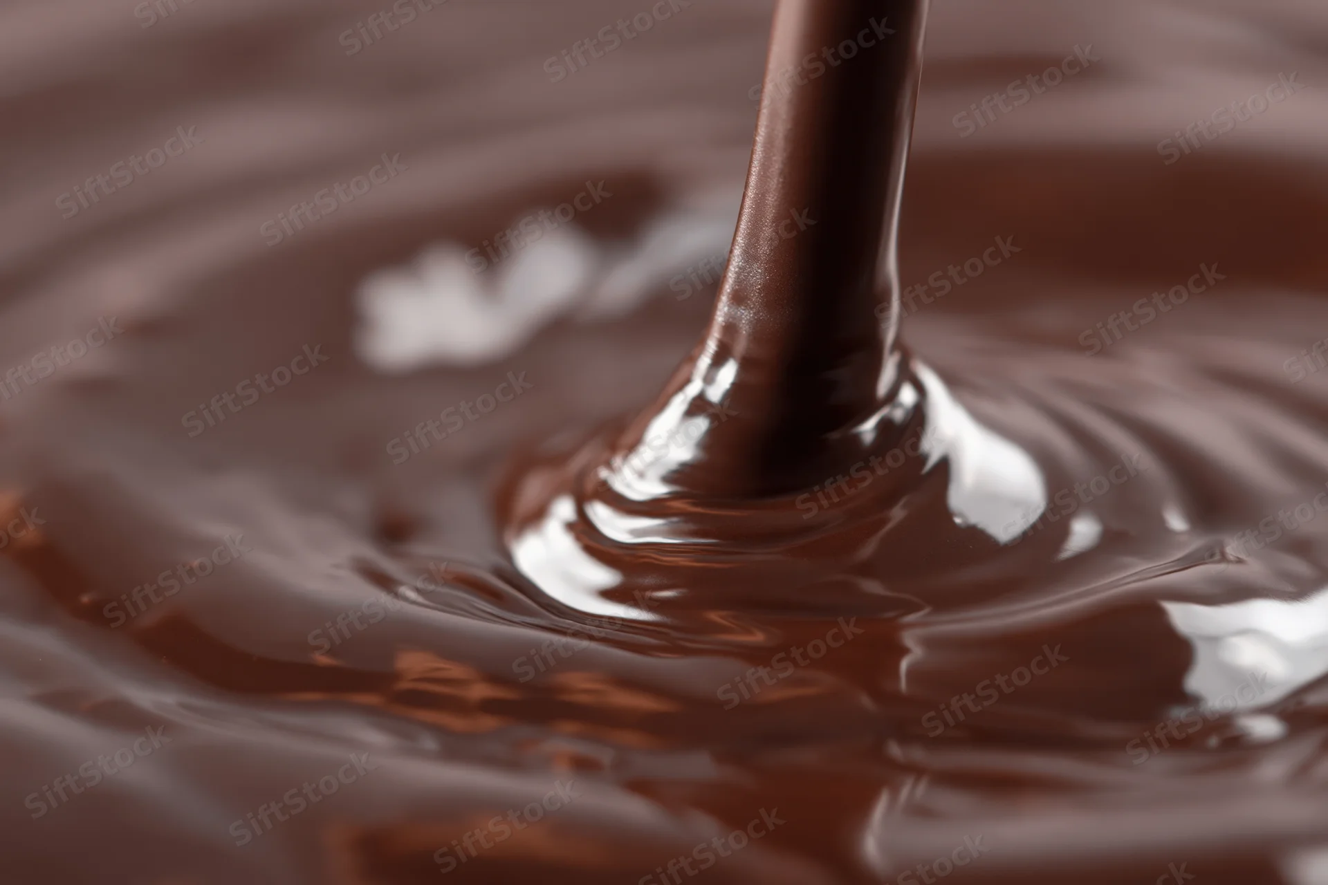 Dark chocolate pouring in a slow stream creating ripples on a glossy surface