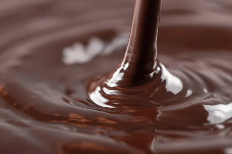 Dark chocolate pouring in a slow stream creating ripples on a glossy surface