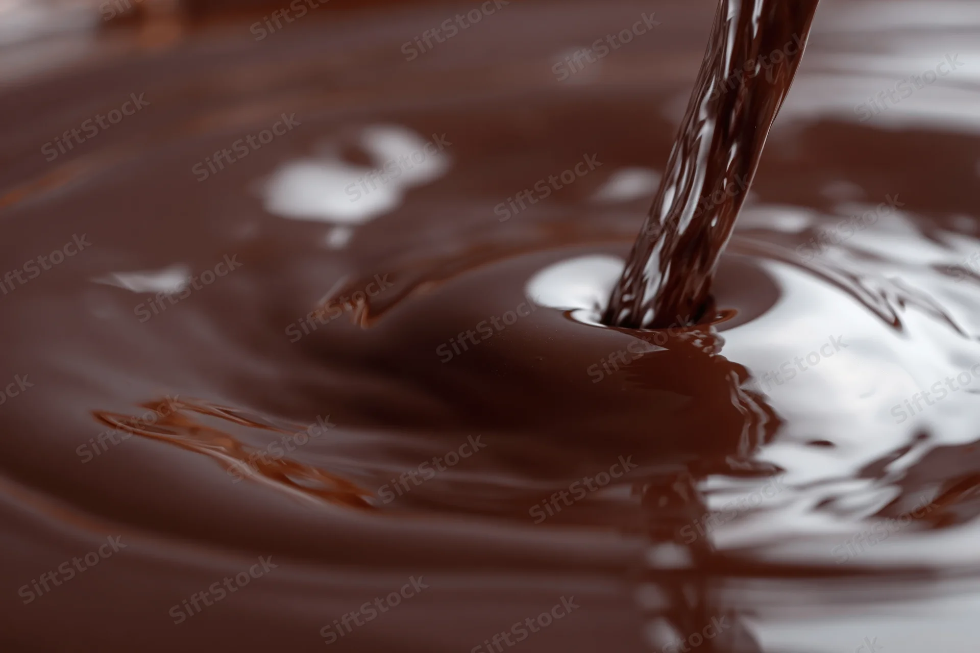 Dark chocolate pouring in a slow stream onto a glossy surface creating ripples and reflections
