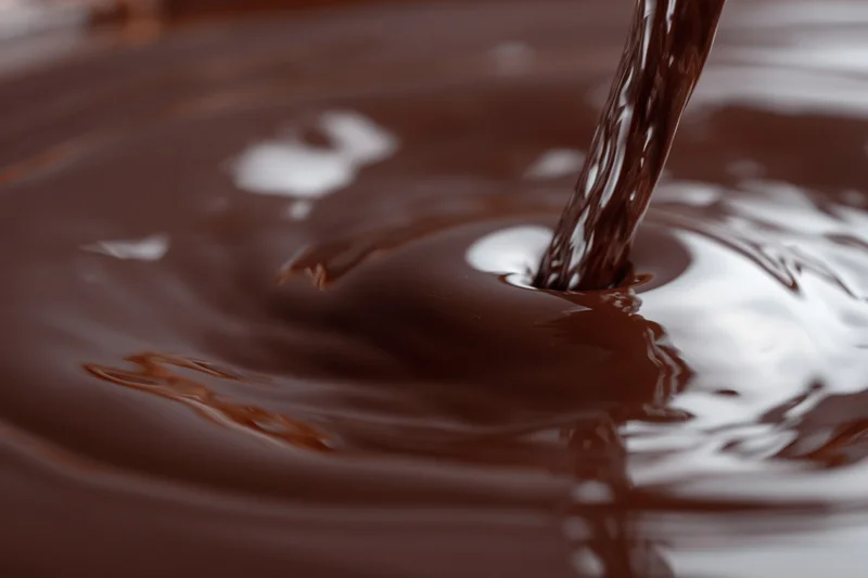 Dark chocolate pouring in a slow stream onto a glossy surface creating ripples and reflections
