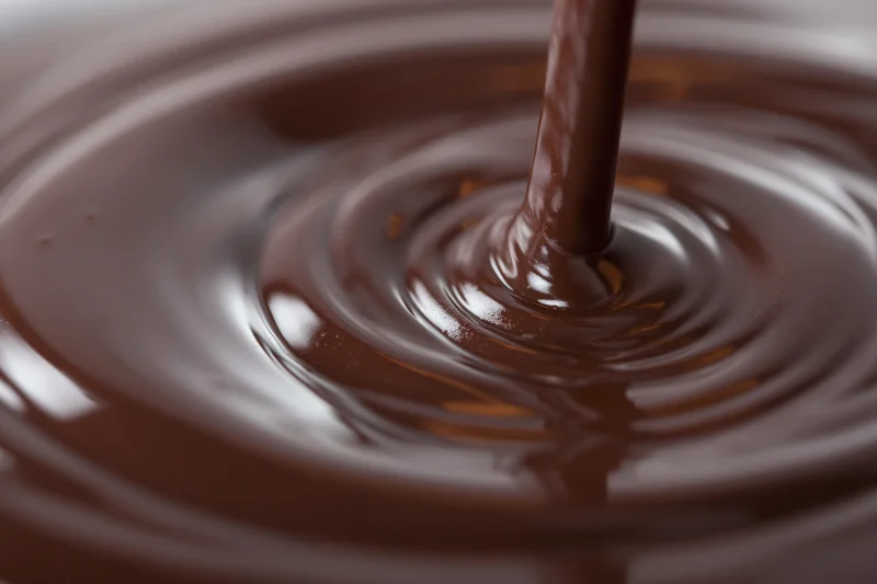 Melted dark chocolate pouring in a slow stream creating ripples on a glossy surface