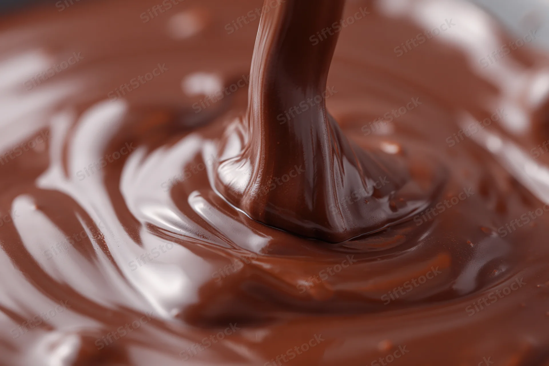 Thick stream of melted dark chocolate pouring onto a smooth surface, creating swirling ripples and glossy texture