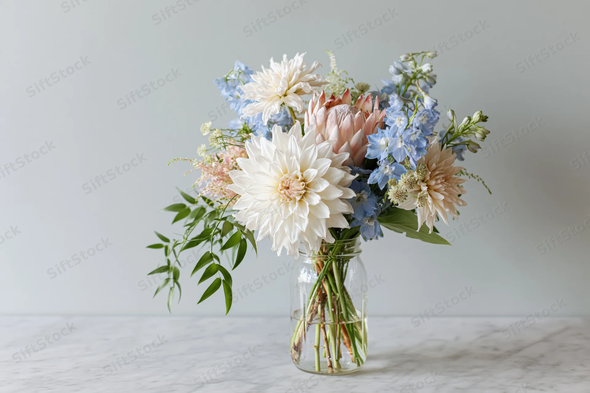 Mixed floral arrangement in a clear glass jar on a marble table