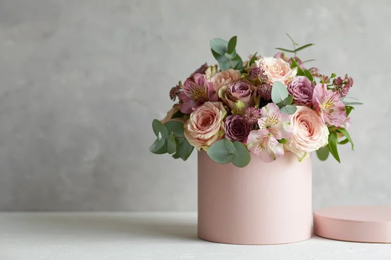 Mixed flower bouquet with roses alstroemeria and eucalyptus in a pink cylindrical box on a white surface