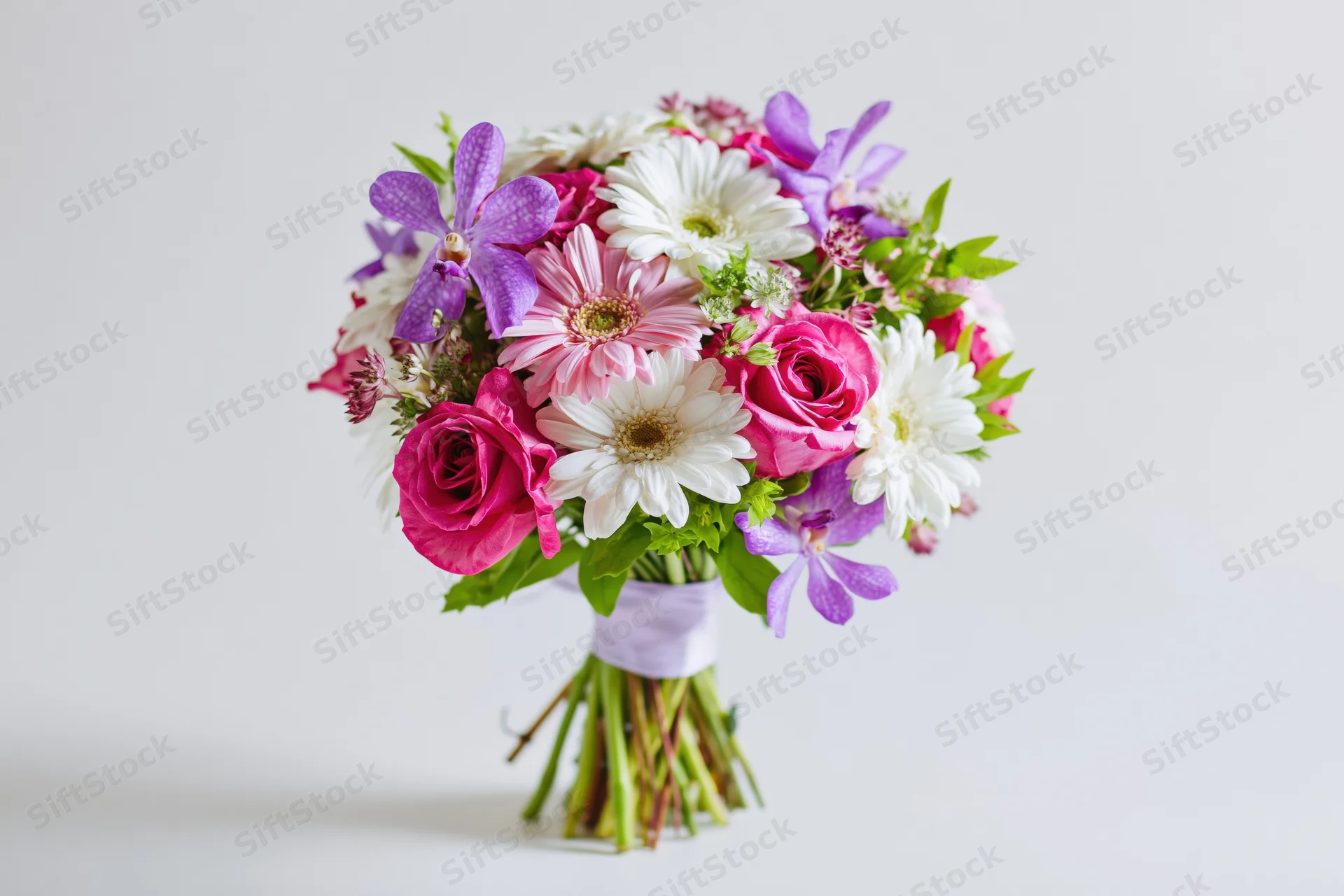 Mixed flower bouquet with pink roses, purple orchids and white daisies wrapped in ribbon against white background