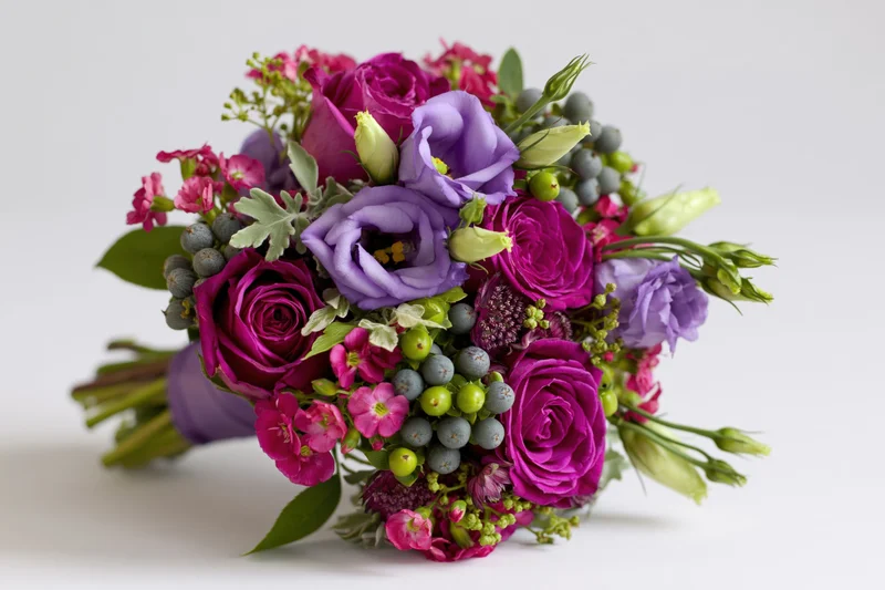 A bouquet of deep magenta roses and lilac lisianthus with greenery and berries on a white background