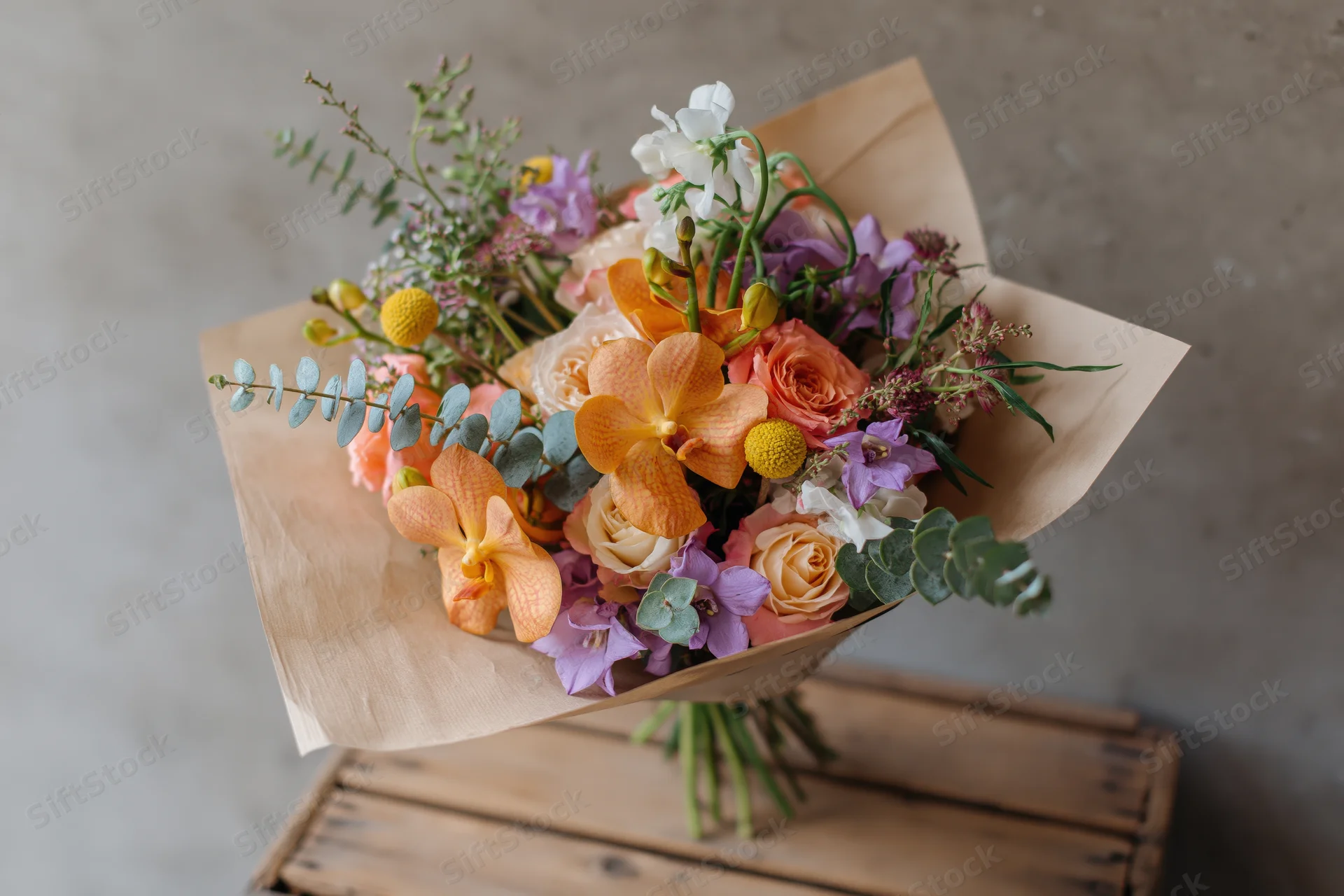 Mixed flower bouquet wrapped in kraft paper resting on wooden crate