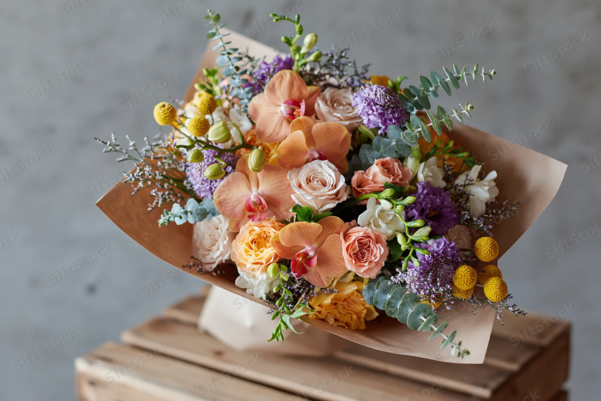 Mixed flower bouquet wrapped in kraft paper resting on wooden crate