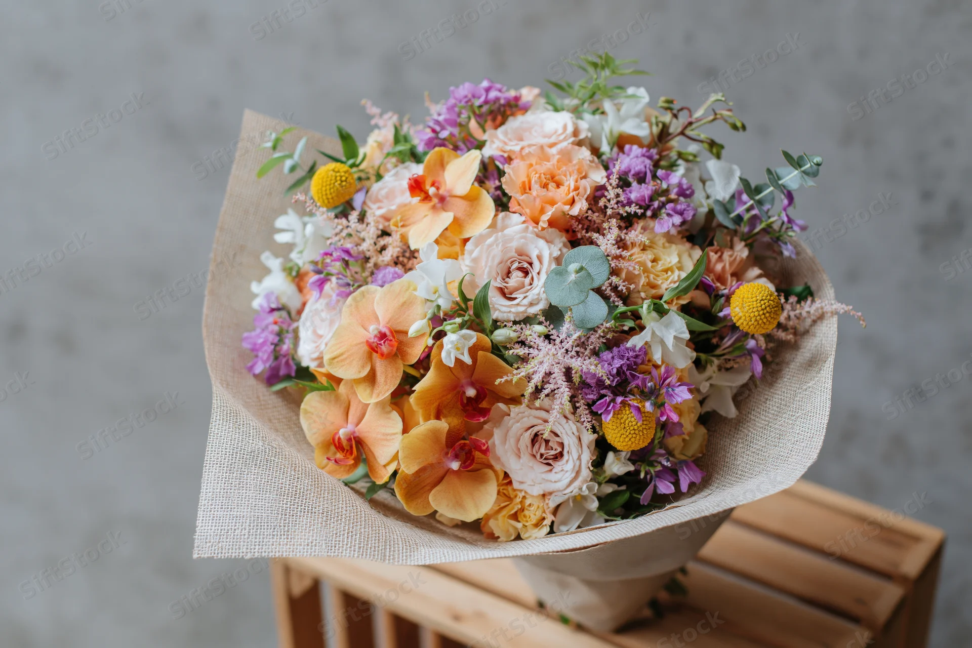 Mixed flower bouquet wrapped in kraft paper resting on wooden crate