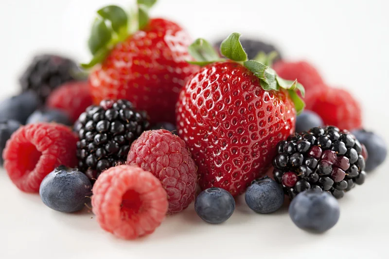 Mixed fresh berries piled together on a white surface