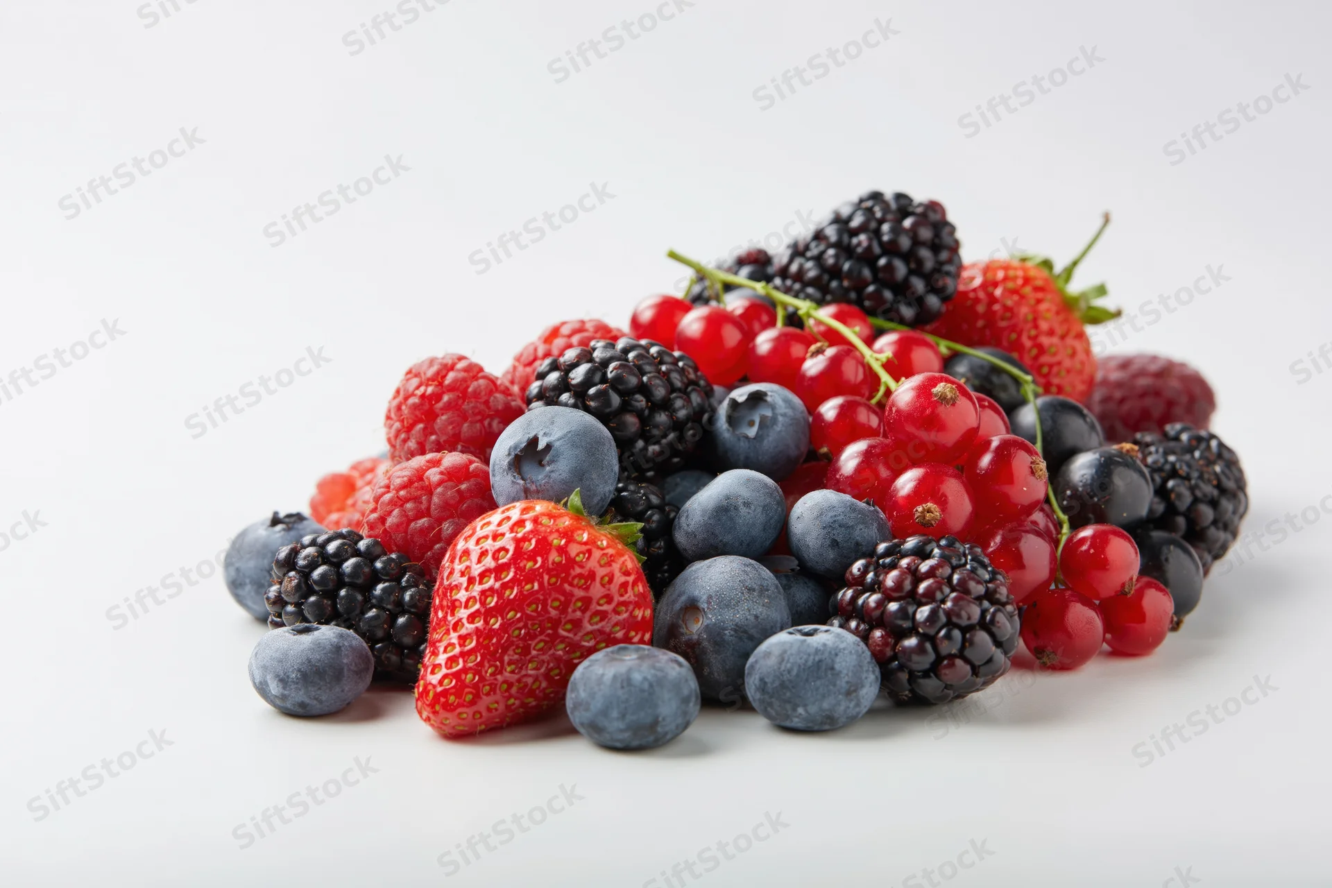 A pile of mixed fresh berries including strawberries, blueberries, blackberries, raspberries and redcurrants on a white surface