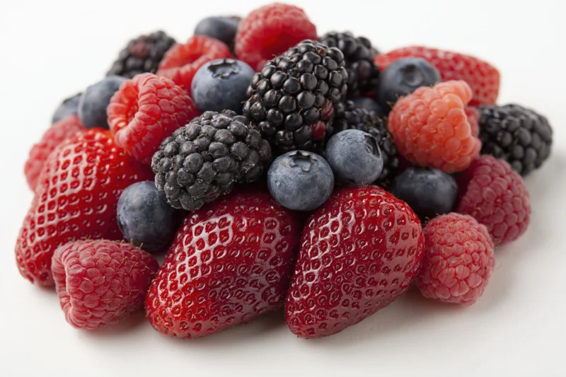 Mixed fresh berries piled together on white background