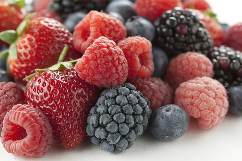 Mixed fresh berries piled together on white surface