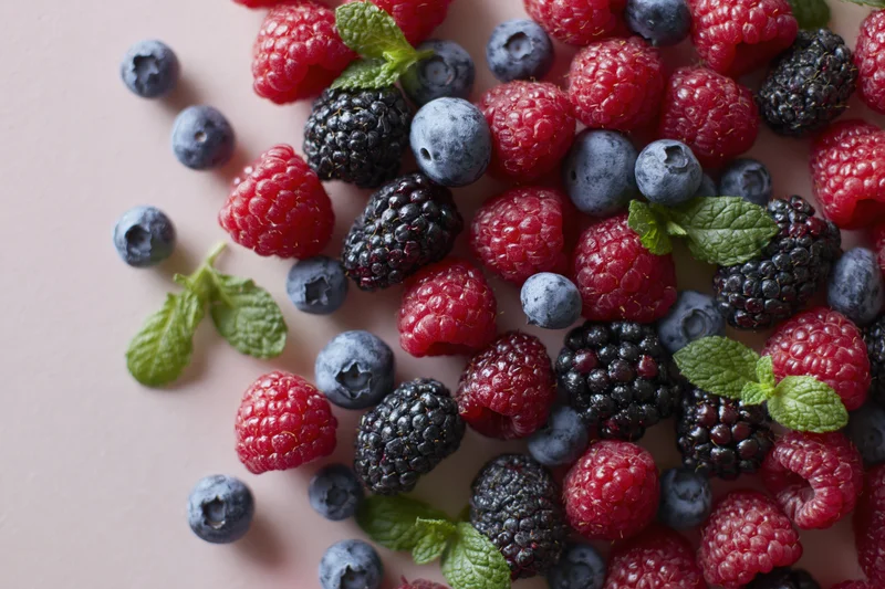 Mixed fresh berries with mint leaves arranged on a pink surface
