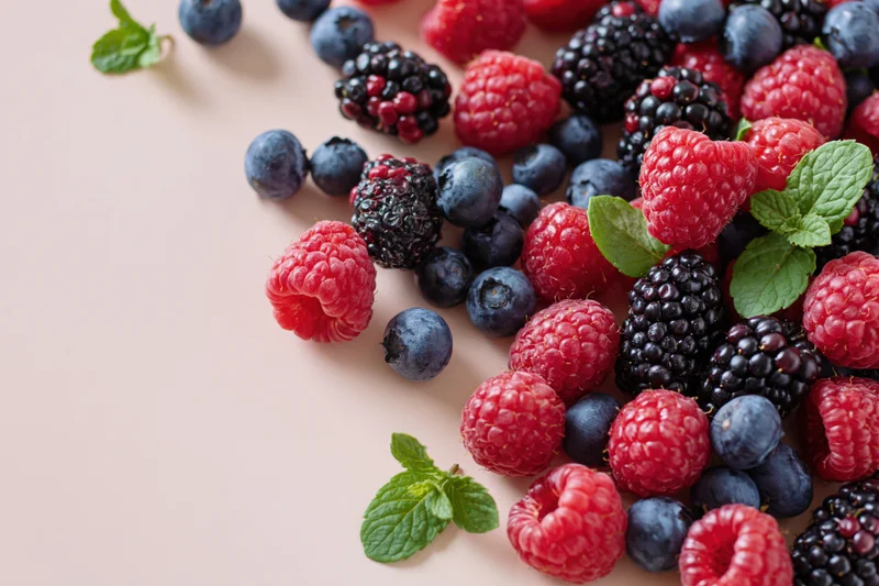 Mixed fresh berries with mint leaves arranged on a pale surface