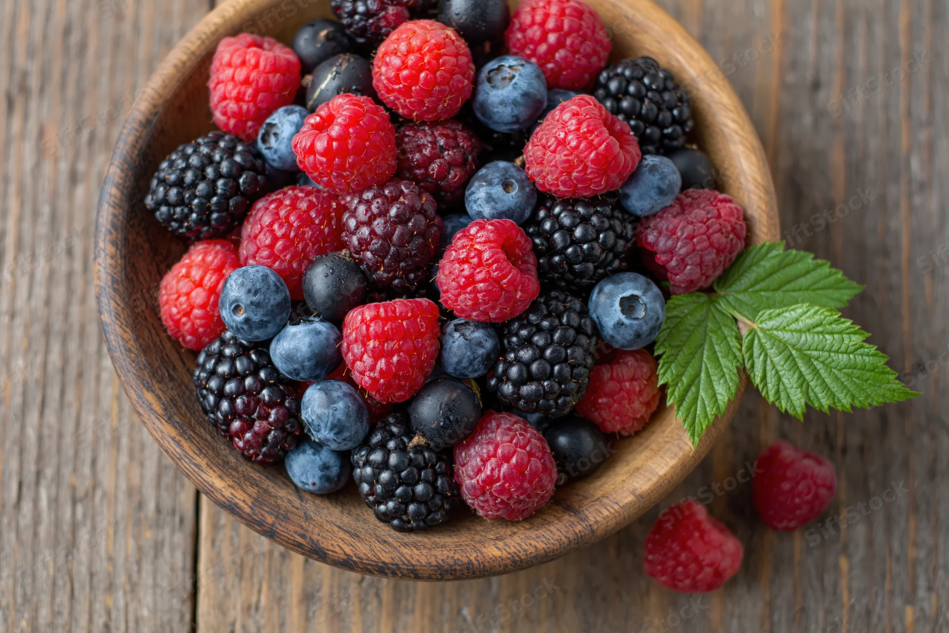 Mixed fresh berries in a wooden bowl on a rustic wooden table