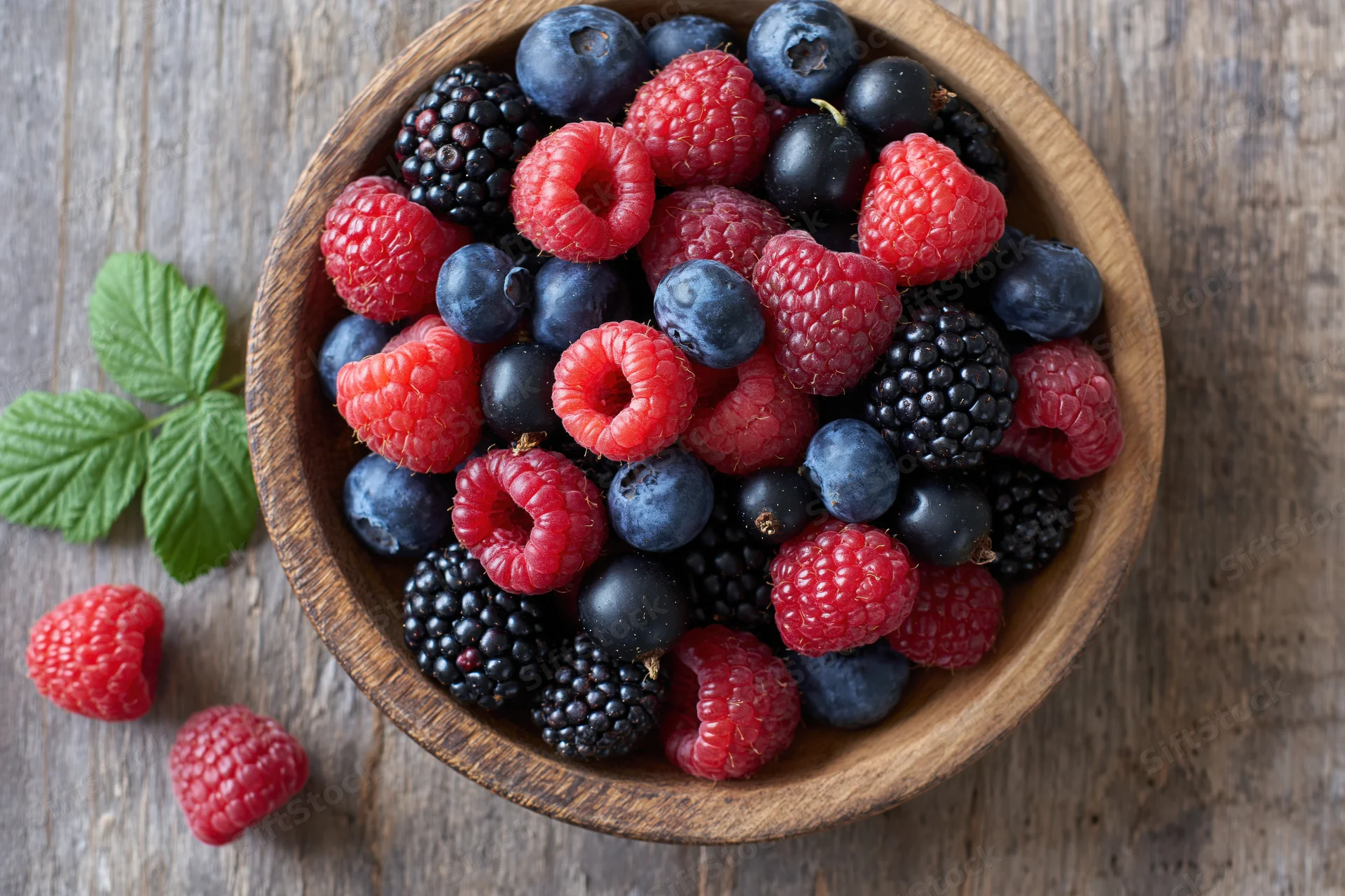 Mixed fresh berries in a wooden bowl on a rustic wooden table