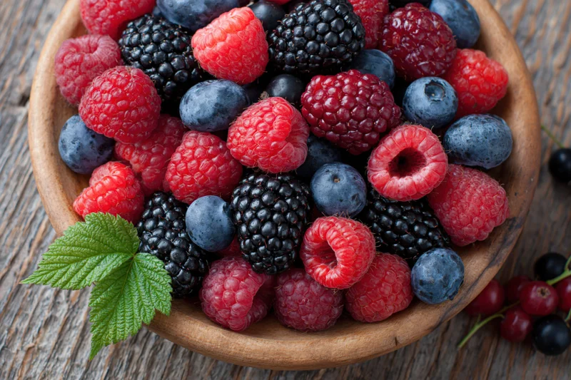 Mixed fresh berries in a wooden bowl on a rustic wood surface