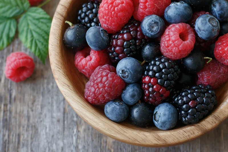 Mixed fresh berries in a wooden bowl on a rustic table