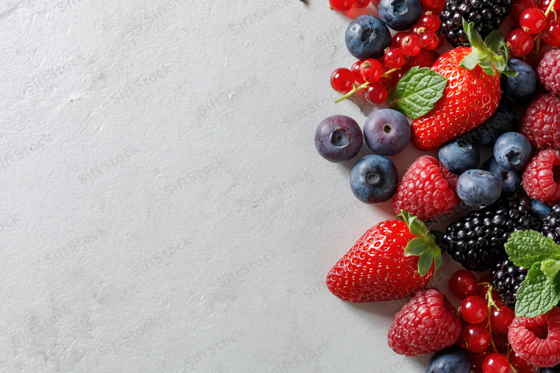 Mixed fresh berries arranged along the right edge of a white surface with copyspace on the left