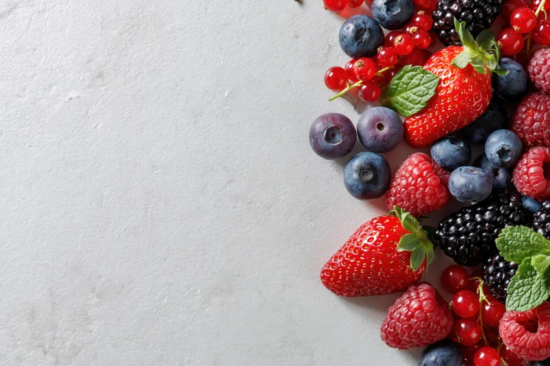 Mixed fresh berries arranged along the right edge of a white surface with copyspace on the left