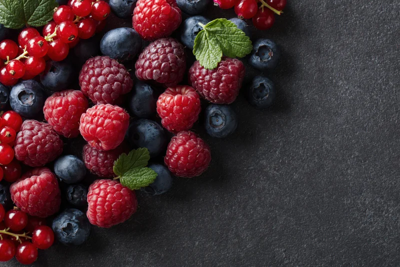 Fresh raspberries, blueberries and redcurrants scattered on a dark charcoal surface with copyspace