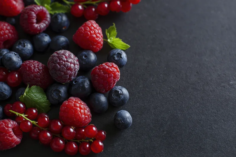Mixed fresh berries scattered on dark charcoal surface with copyspace