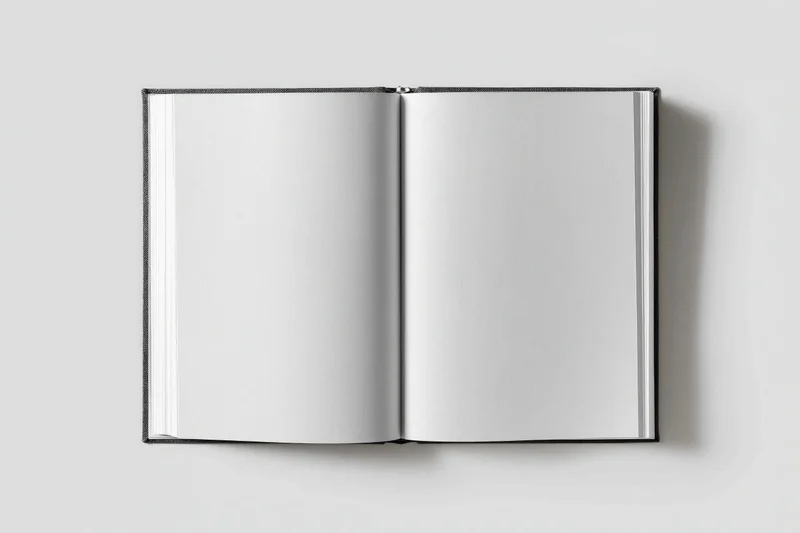 Open hardcover book with blank white pages lying flat on a neutral surface
