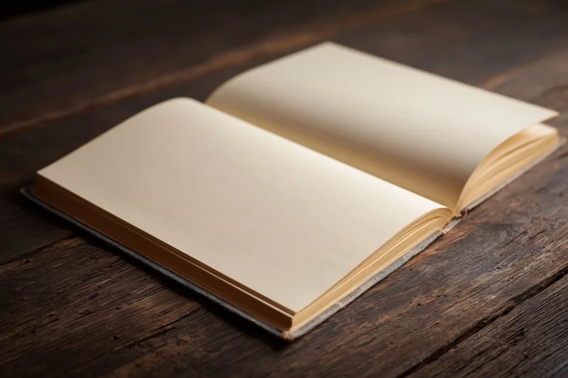 Open hardcover book with blank cream pages lying flat on dark wooden table