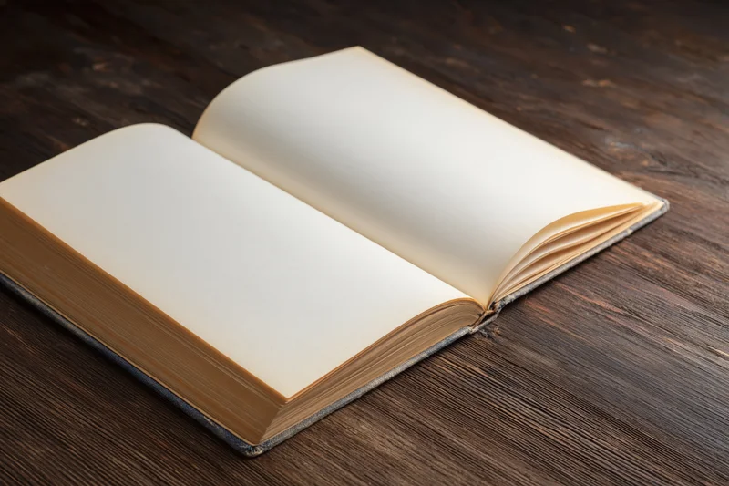Open hardcover book with blank cream pages lying flat on dark wooden table