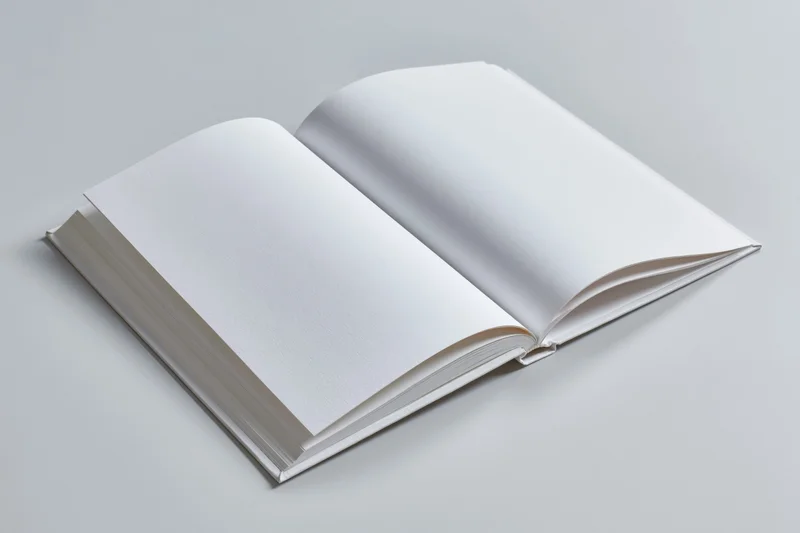 Open hardcover book with blank white pages lying flat on a light surface