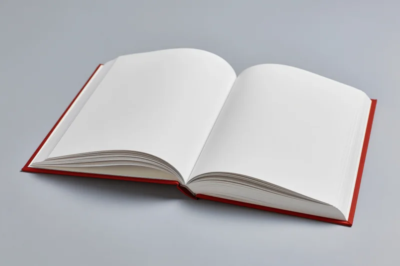 Open hardcover book with blank white pages lying flat on a neutral surface