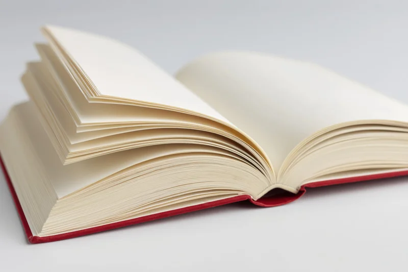 Open hardcover book with red binding lying flat and pages fanned on white background