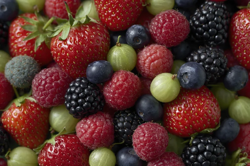 Overhead close-up of a dense pile of mixed fresh berries including strawberries, raspberries, blueberries, blackberries, and gooseberries