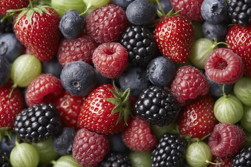 Overhead close-up of a dense pile of mixed fresh berries including strawberries, raspberries, blueberries, blackberries and gooseberries
