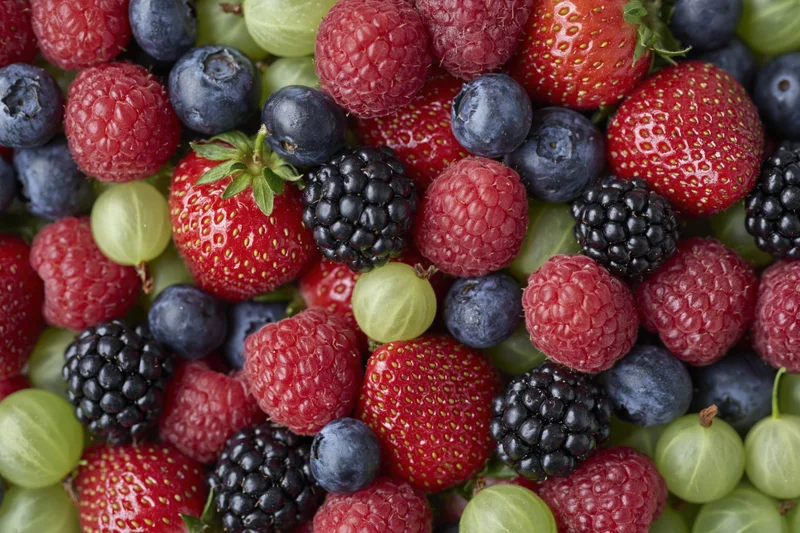 Overhead close-up of a dense pile of mixed fresh berries including strawberries, raspberries, blueberries, blackberries and gooseberries