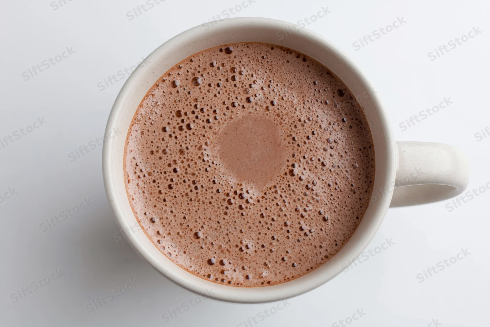 Overhead view of a white ceramic mug filled with frothy hot chocolate on a plain white surface