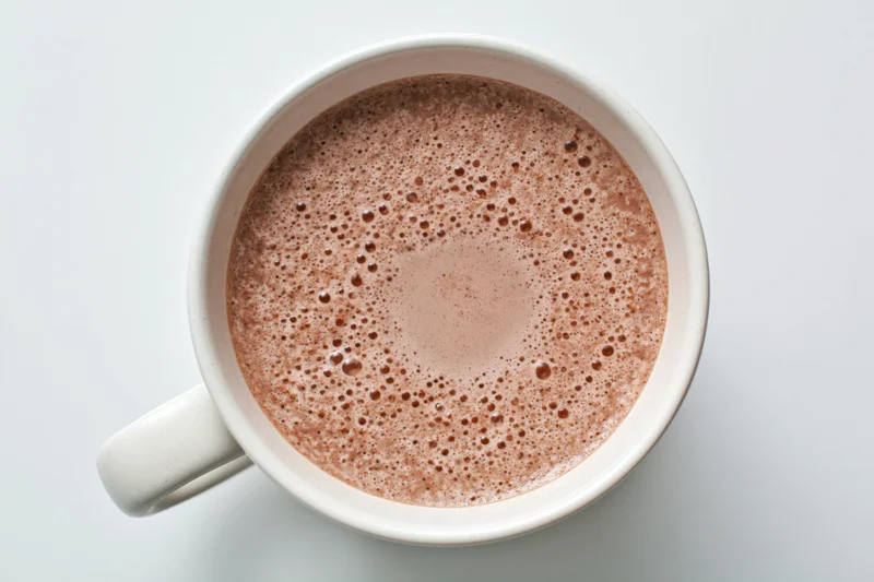 Overhead view of a white ceramic mug filled with frothy hot chocolate on a plain white surface