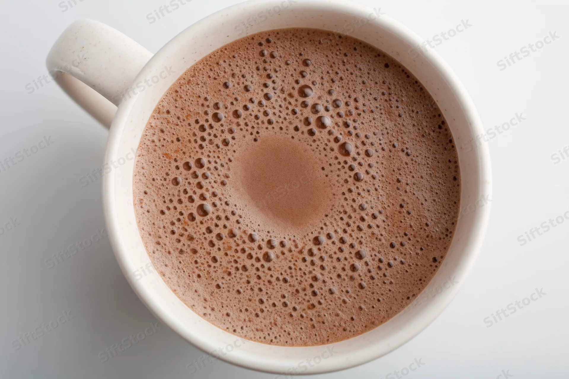 Overhead view of a white ceramic mug filled with frothy coffee on a plain surface