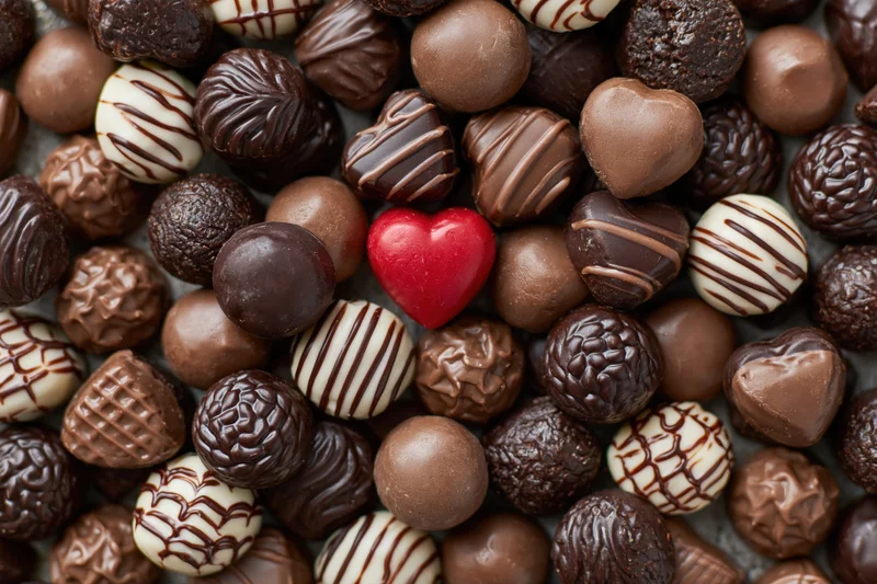 Overhead flat lay of assorted chocolate pralines with a red heart-shaped candy in the center