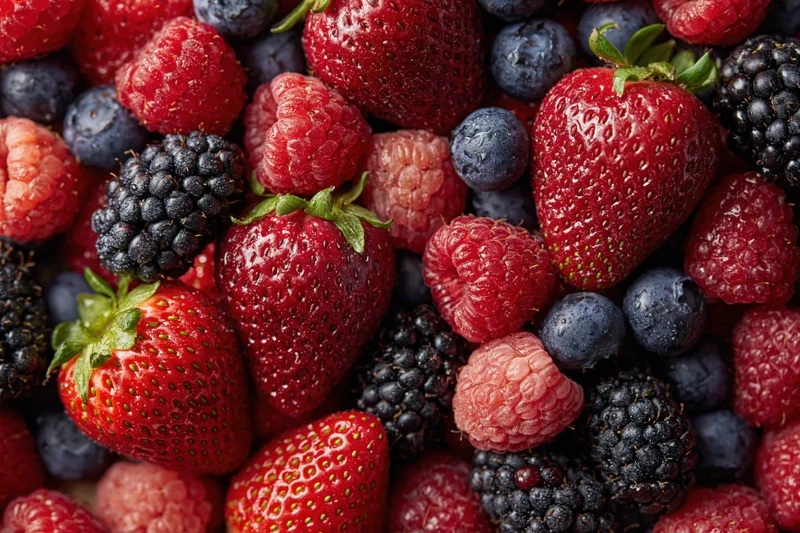 Overhead closeup of fresh mixed berries including strawberries raspberries blueberries and blackberries arranged in a flat lay