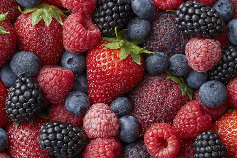 Overhead closeup of fresh mixed berries including strawberries raspberries blueberries and blackberries arranged in a flat lay