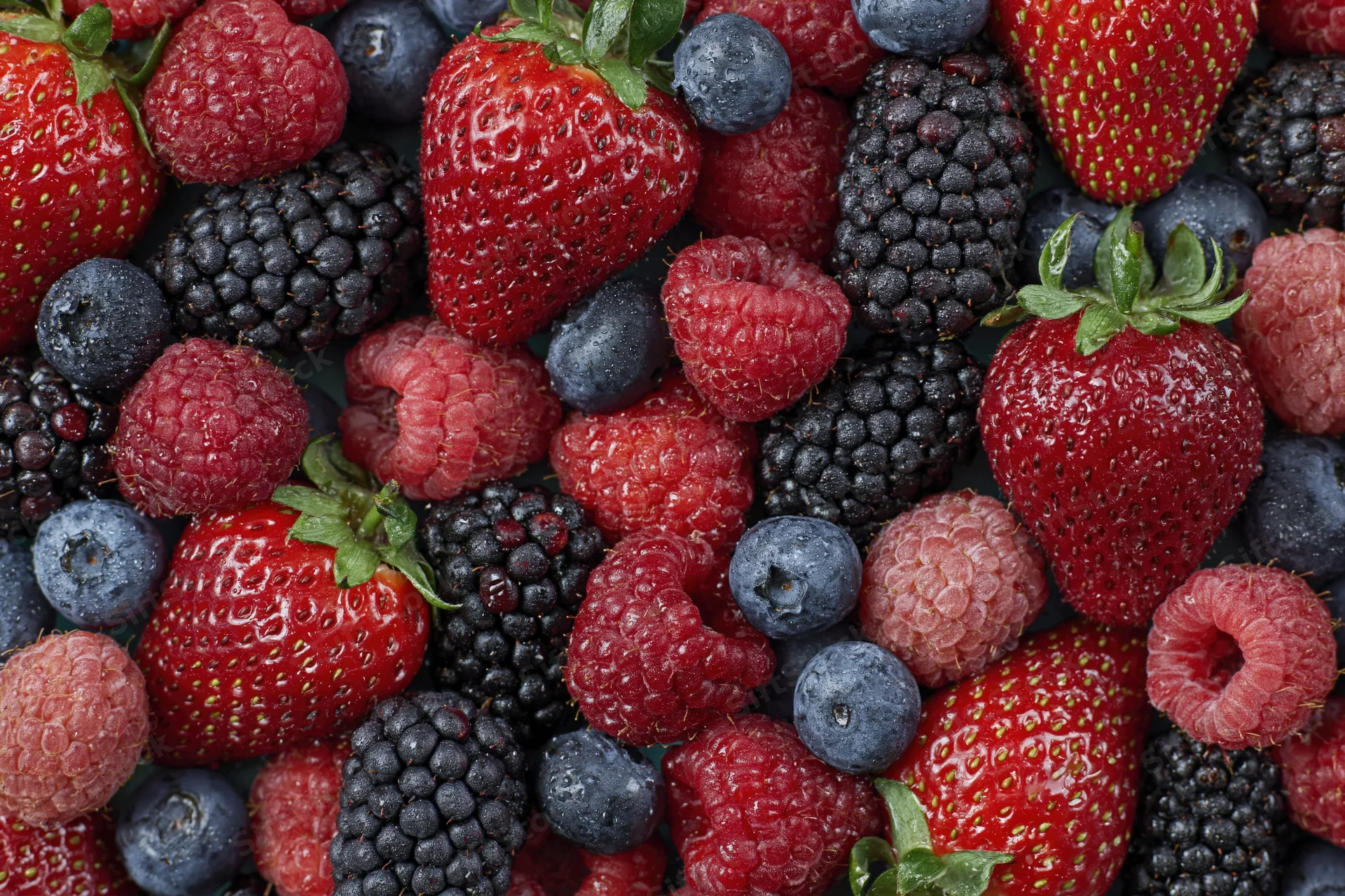 Overhead flat lay of fresh mixed berries including strawberries raspberries blueberries and blackberries
