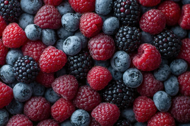 Overhead closeup of mixed fresh berries covering the entire frame in a flat lay arrangement